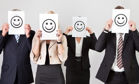 A line of people in business attire holding up smiley faces in front of their faces